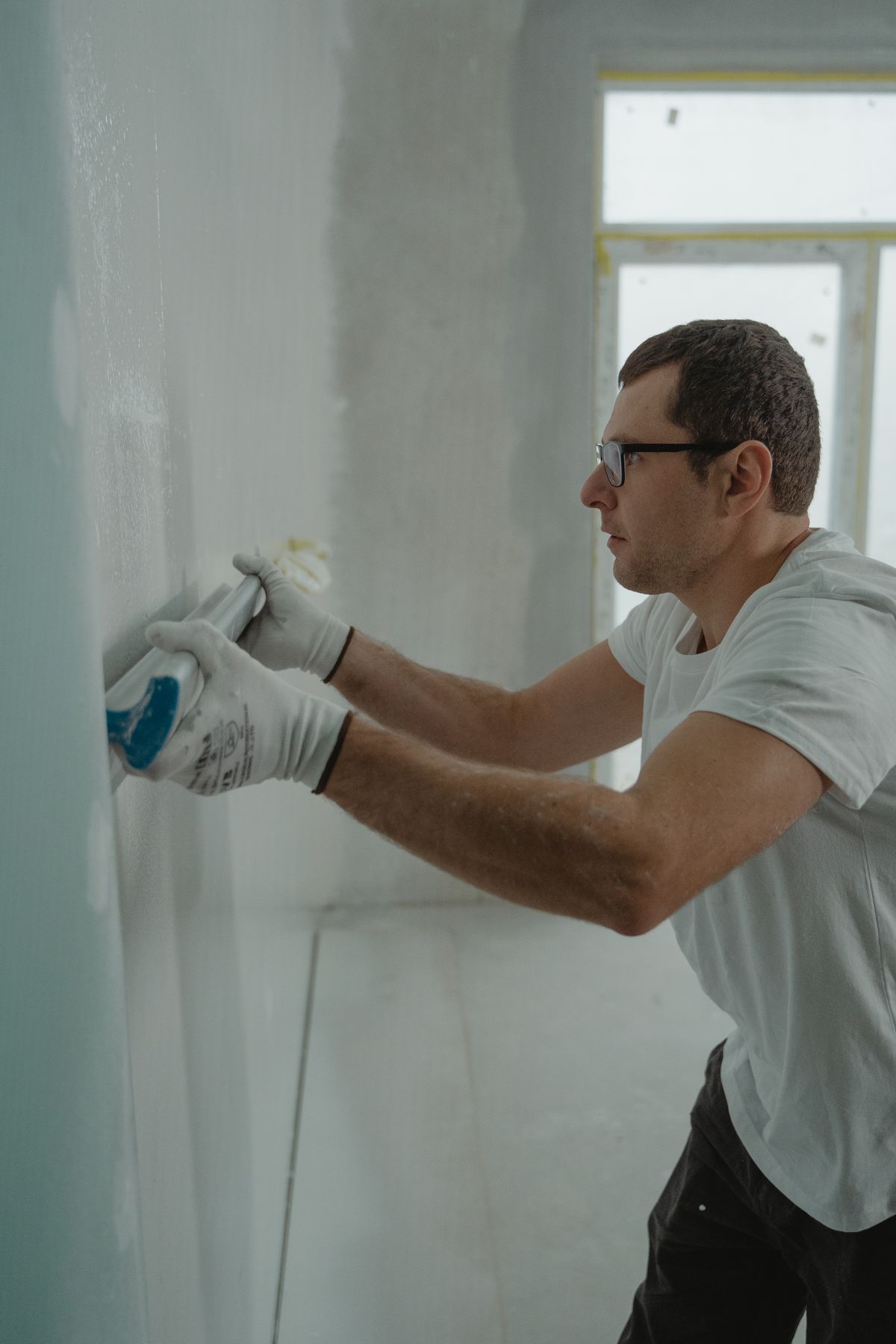 Drywall finisher pressing joint compound into a repaired wall surface with a taping tool