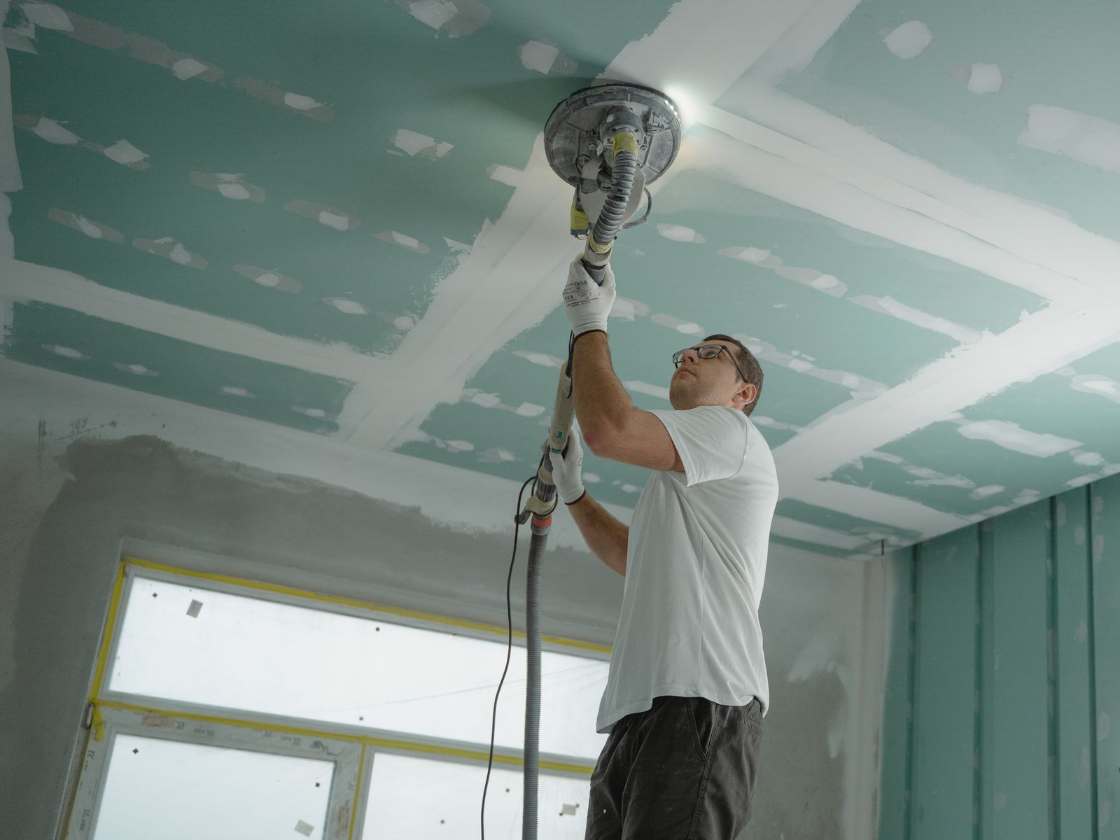 Drywall professional smoothing a ceiling with a dust-extracting sander after texture removal